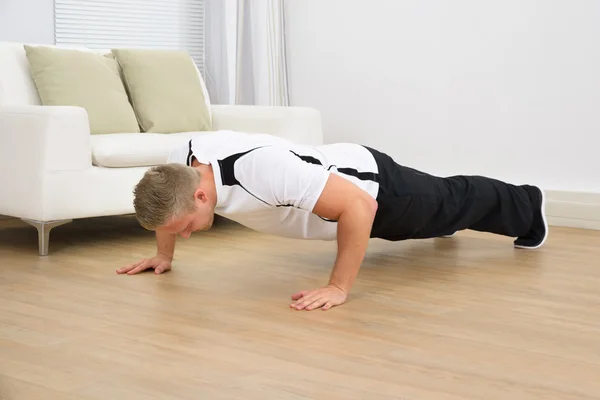 A man performing a push-up exercise on a wooden floor in a living room setting. Push-ups are a simple exercise that can be done at home to build upper body strength and improve fitness.